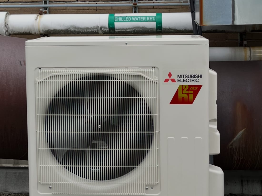 New Mitsubishi Electric outdoor heat pump unit installed on a commercial building beside chilled water pipes
