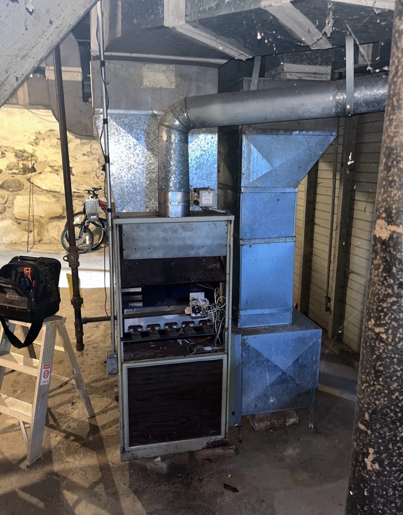 Gas furnace opened up for repair with a ladder and tool bag beside it