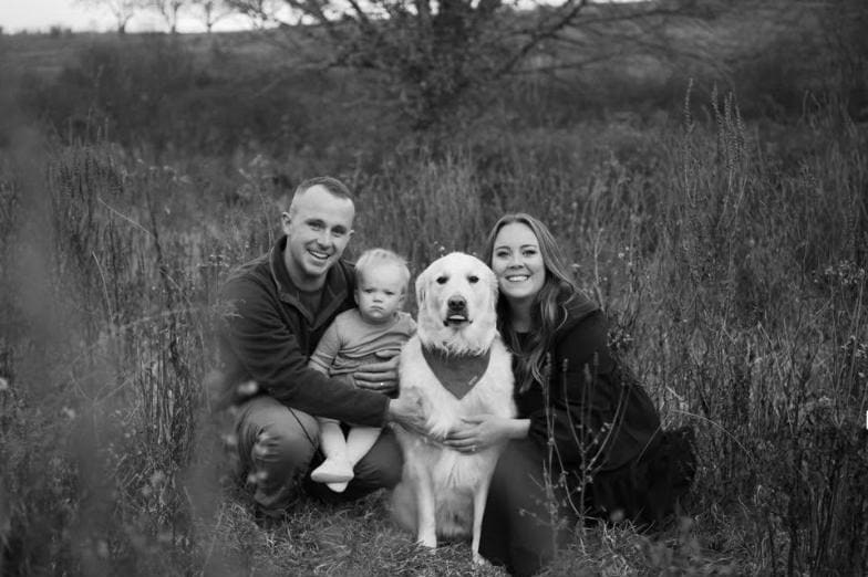 Derek Neary and his family kneeling together in a field with their golden retriever