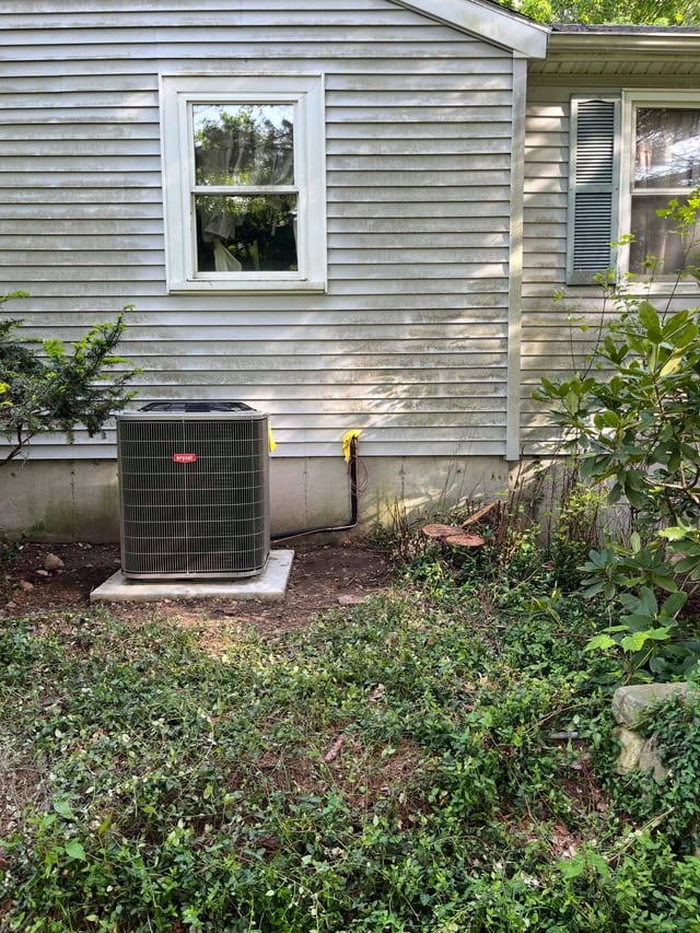 New outdoor condenser on a pad beside gray siding and a window