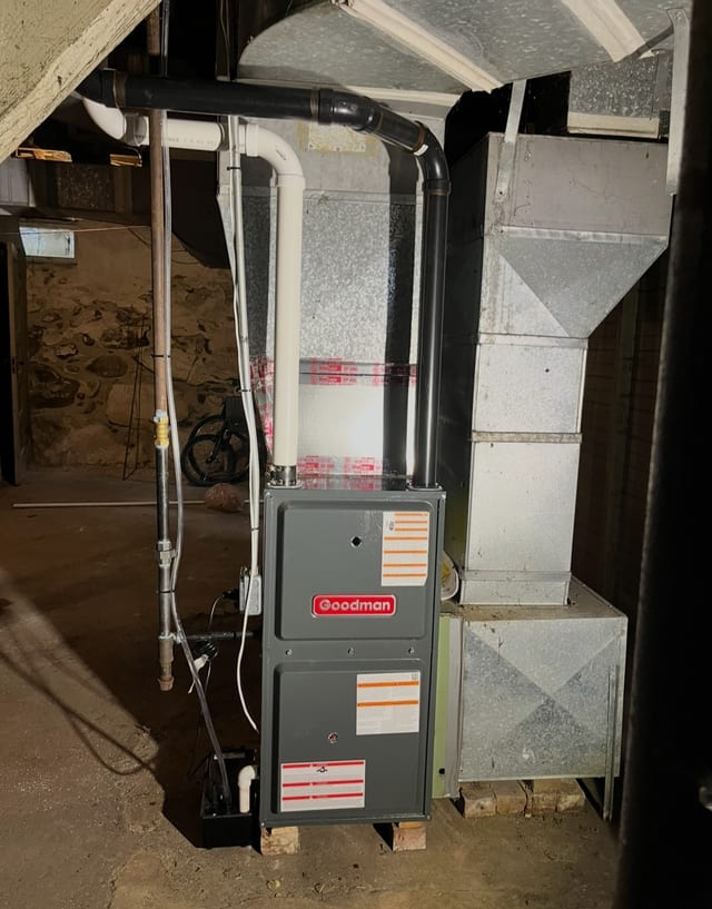 Goodman furnace with new white PVC pipes and a large duct plenum in a basement