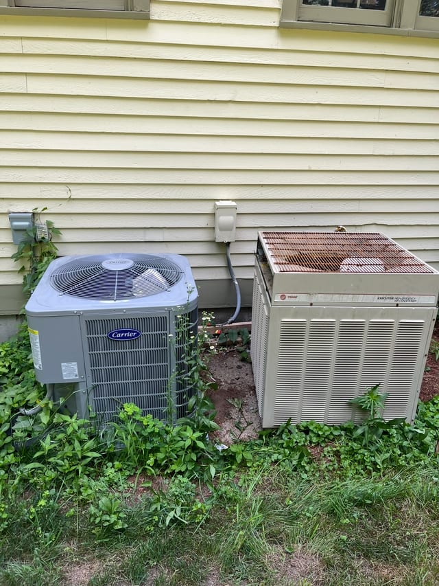 Two outdoor condensers beside a yellow sided house